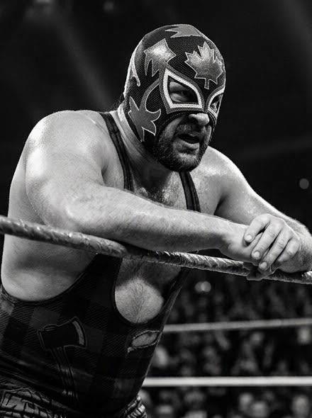 Black and white portrait of The Timberman leaning on the ring ropes, staring down the crowd
